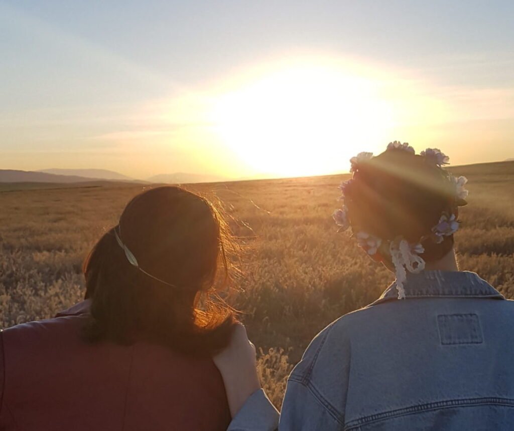 two friends standing in poppy fields watching the sunset