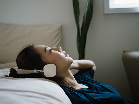 Teenager asian woman listening to music whit her headphone while lying on bed in bedroom at home